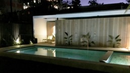 corner view of Freshwater pool with fencing, deck and sun chairs at night